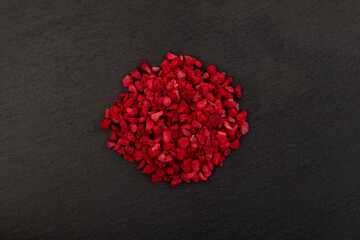 Pile of Freeze dried raspberries nibs on dark stone surface, top view. Dehydrated raspberry. Clever Storage healthy food. Dried fruit. Delicious topping for porridge, cereal, yogurt and desserts