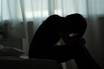 Depressed man sitting alone on the bed with hands on head feel stress, sad and worried in the dark bedroom and low light environment
