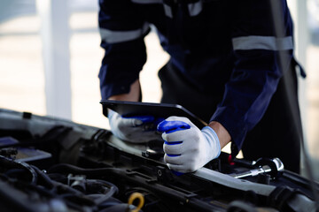 A mechanic is working on a car with a tablet in his hand. Concept of focus and concentration as the mechanic uses the tablet to diagnose and repair the vehicle