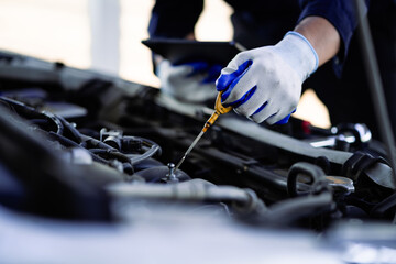A mechanic is checking the oil in a car. The oil is low and the mechanic is adding more