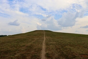 The green grass hill landscape with the clouds in the sky.