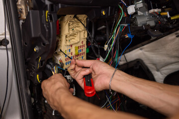 Closeup image featuring hands fixing electrical wires in a car for maintenance and repair