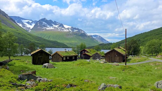 A tranquil video showcases a picturesque village in the mountains with a serene lake, charming wooden houses, green roofs in a valley, and a peaceful mountainous setting, Innerdalen valley Norway