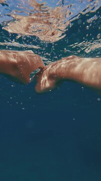 POV shot, split level, guy paddling with his hands underwater to rocky shore