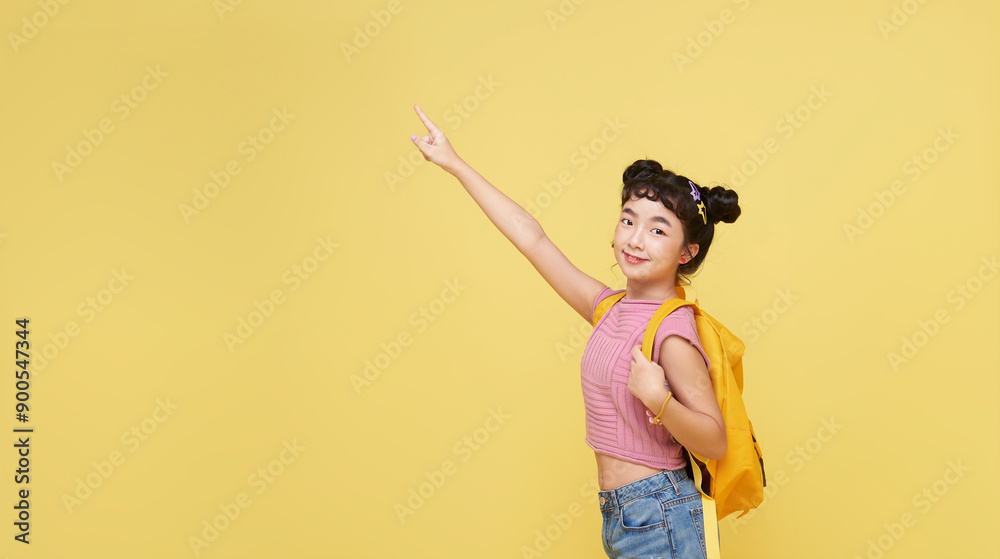 Canvas Prints happy young Asian student elementary school girl and backpack ready to school pointing finger up isolated on yellow copy space background.