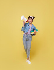 Young Asian student woman shouting into megaphone making announcement in isolated on yellow...
