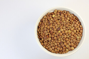 Bowl overflowing with nutritious brown lentils on a white background, perfect for plant-based diets. Rich in protein and fiber, lentils are ideal for vegetarian and vegan dishes