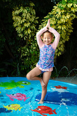 Cute Caucasian little girl doing yoga at the splash pad. Tree pose child. Summer fun kids concept