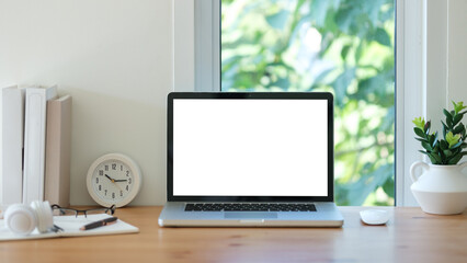 Laptop with white blank screen, books, coffee cup and headphone on wooden table.