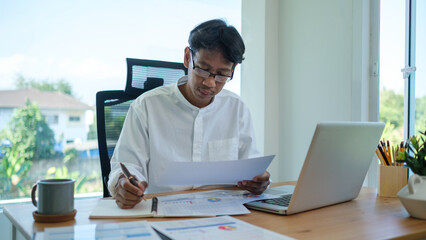 A focused professional working at his desk, reviewing documents and taking notes.