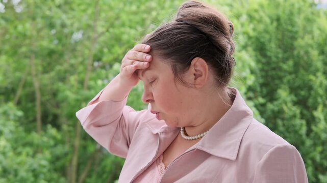 mature woman, 50, elegantly dressed in pink feeling unwell, fans herself, experiencing hot flashes and discomfort from menopause, feminine health issues, aging gracefully