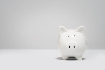 Minimalist photo of a white piggy bank against a plain grey background, symbolizing savings and...