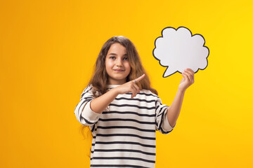 Smiling kid girl holding cloud bubble card and pointing finger at it over yellow background. Dreaming concept