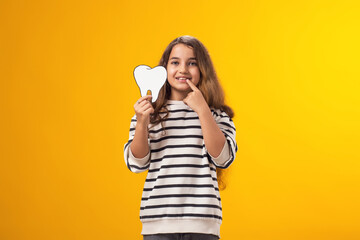 Smiling child girl holding papercraft tooth and pointing at her lost teeth. Dental health concept