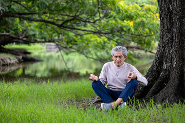 Asian senior man is relaxingly practicing meditation yoga in forest during summer to attain...