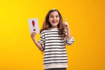 Surprised kid girl holding exclamation point card and pointing finger up. Children, idea and knowledge concept