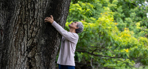 Elder senior asian man is hugging mature tree in the forest for natural energy and electrical grounding in longevity, healthy and happiness connection the mother nature concept