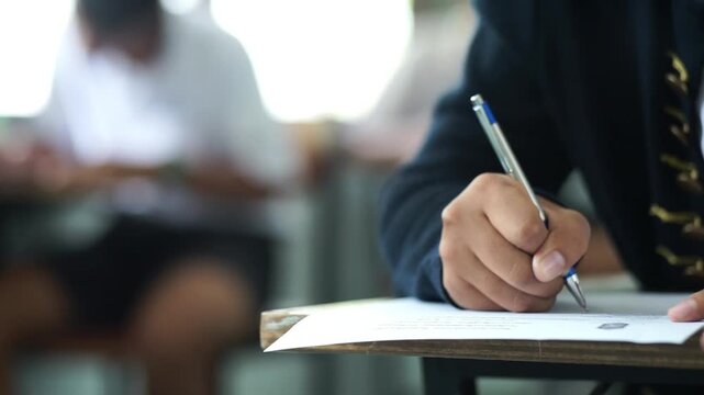 Close up hand of student reading and writing exam answer sheets exercises with stress in classroom