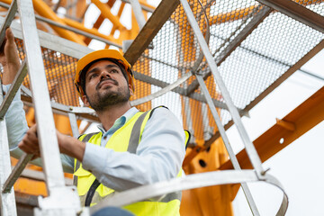 Asian male engineer wearing safety vests and helmet climbing metal ladder inspection and maintenance tower crane at construction site. © Supachai