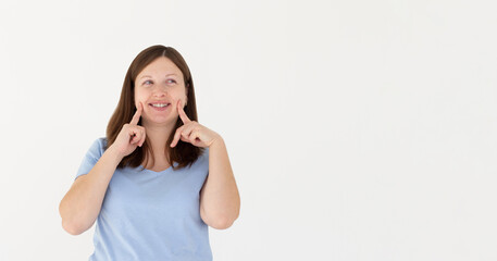 Young brunette woman pointing fingers at her cheeks isolated over white background