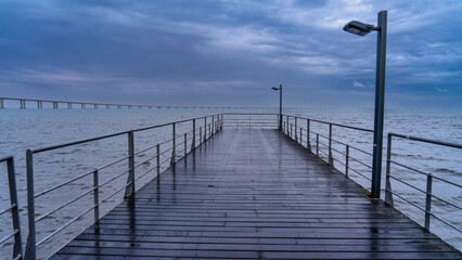 Naklejka premium Pedestrian area in rainy day with Vasco da Gama bridge located in Parque das Naçoes in Lisbon