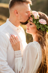 Obraz premium groom in white shirt and pants and bride in white dress kissing close-up
