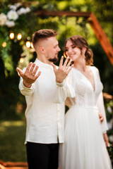 Stylish groom and cute bride in white dress outdoors near wedding wooden arch decorated with flowers. Wedding portrait of newlyweds