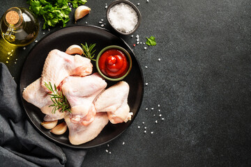 Raw Chicken meat with herbs and spices on black. Different part of chicken - fillet, wings, drumsticks. Top view with copy space.