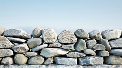 A close-up of a rustic stone wall with various sizes and shapes of grey rocks against a clear blue sky.