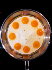 View from above of eight fried eggs in a metal fry pan on a stove