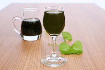 Gotu kola juice in a tall glass, place the leaves and bowl next to it on a light colored wooden table.

