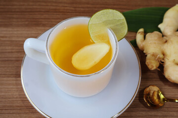Dark yellow liquid floats on slices of ginger. Lemon in white pearl cup with saucer Place on the table with rhizomes and leaves.

