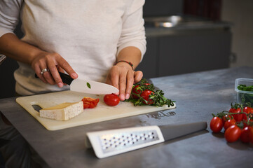 Close-up of hands slicing tomatoes on a cutting board in a modern kitchen