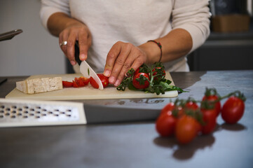 Close-up of hands chopping fresh tomatoes and cheese in a modern kitchen setting
