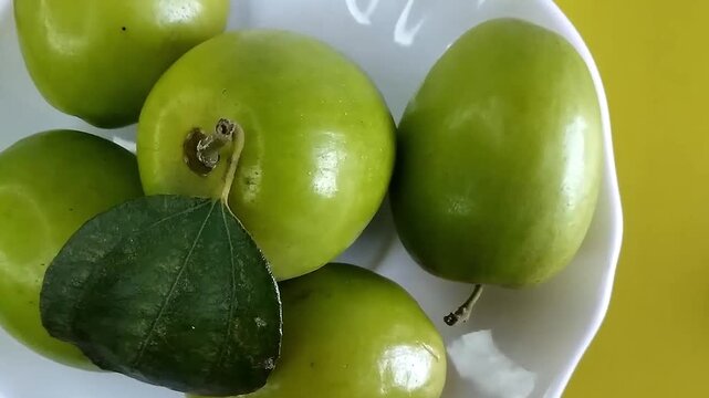 Top view close up of ripe green jujube fruit on a white plate against yellow background. Rotating indian jujube ziziphus mauritiana fruit concept.