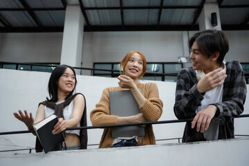 Three asian students happily discussing during a break at university, surrounded by books and...
