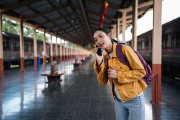 Young woman is standing on a train platform, talking on her phone and waiting for her train to arrive