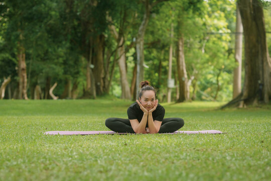 Young woman is practicing yoga in a park, sitting on a yoga mat in a bound angle pose
