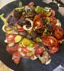 a mixture of chopped meat, tomatoes, onions, peppers, potatoes, and eggplant is cooked in a pan of oil