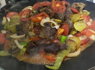 a mixture of chopped meat, tomatoes, onions, peppers, potatoes, and eggplant is cooked in a pan of oil