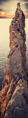Obraz premium Couple Standing on High Rocky Cliff Overlooking Ocean at Sunset