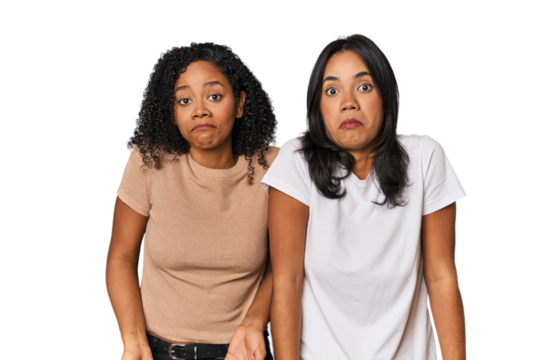 Young Latin friends in studio shrugs shoulders and open eyes confused.