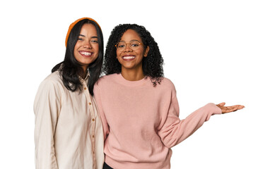 Young Latin friends together in studio showing a copy space on a palm and holding another hand on waist.