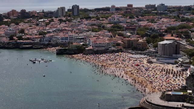Aerial drone view of crowded Conceicao Beach in Cascais, Portugal on a sunny summer day