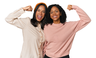 Young Latin friends together in studio showing strength gesture with arms, symbol of feminine power