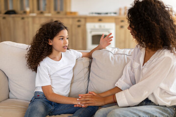 Preteen daughter talking with her mother, mum consoling quiet girl, giving love, comfort, support, touching hand of child at home. Psychology, therapy concept