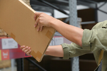 Hands holding a large cardboard box, focusing on the secure grip and handling technique in a warehouse environment. Emphasizes the careful management and movement of inventory items.