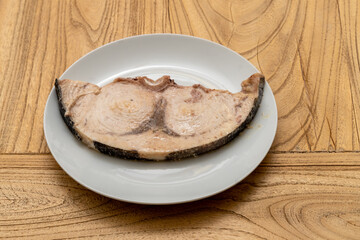 a grilled swordfish fillet on a white plate on a wood table