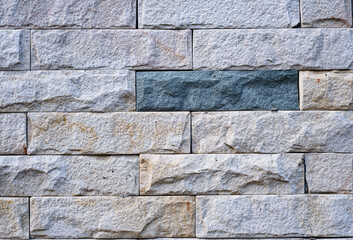 A wall made of gray and white bricks with a blue brick in the middle. The wall is very old and has a rustic feel to it