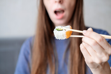 A young woman with long hair holds rolls on sticks against the background of an open mouth, close-up